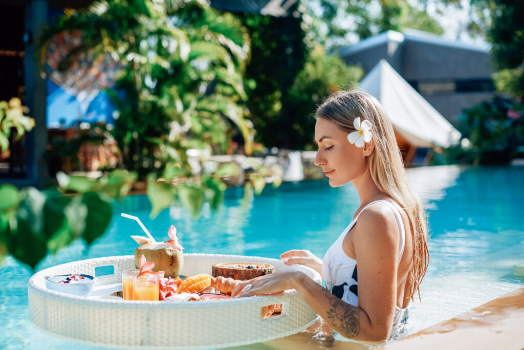 Female tourist in luxurious hotel enjoys swimming pool and tropical food